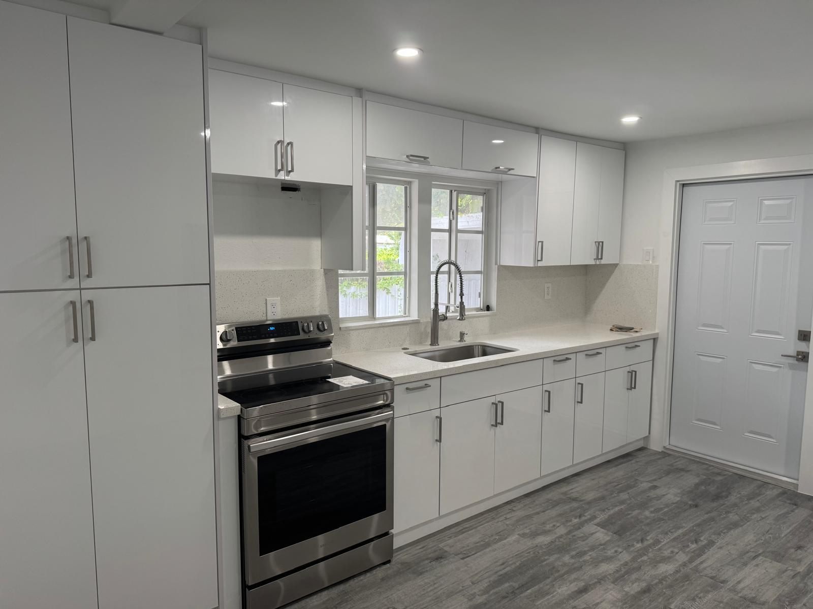 Cocina blanca con gabinetes hasta el techo, encimera de cuarzo y piso laminado