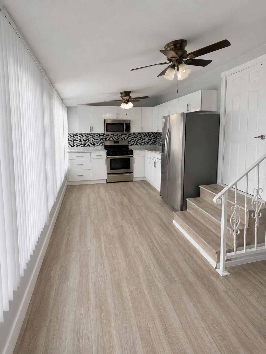 Cocina abierta con piso laminado, gabinetes blancos y electrodomésticos de acero